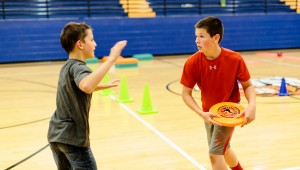 a boy with a frisbee playing a game with another boy in a gym