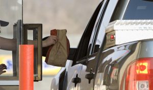 Arby’s restaurant worker handing a customer in a pick-up truck a bag of food at their drive through window.