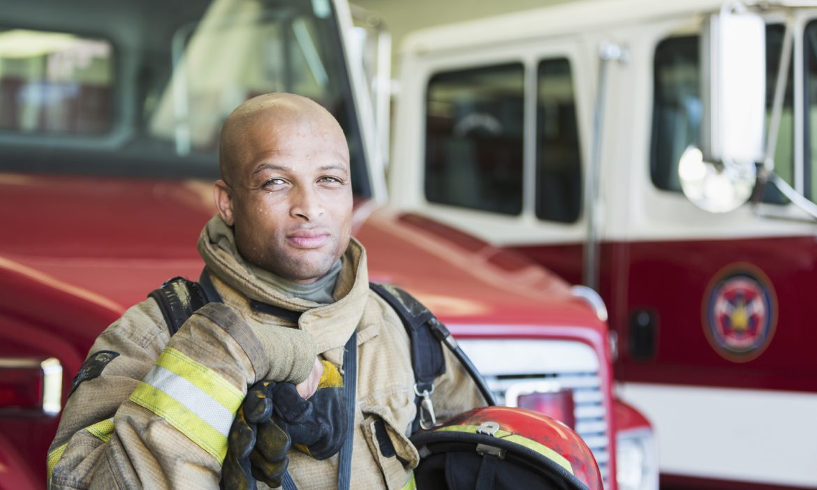 Portrait of an African American fireman standing in front of a fire engine parked at the station.