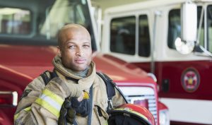 Portrait of an African American fireman standing in front of a fire engine parked at the station.