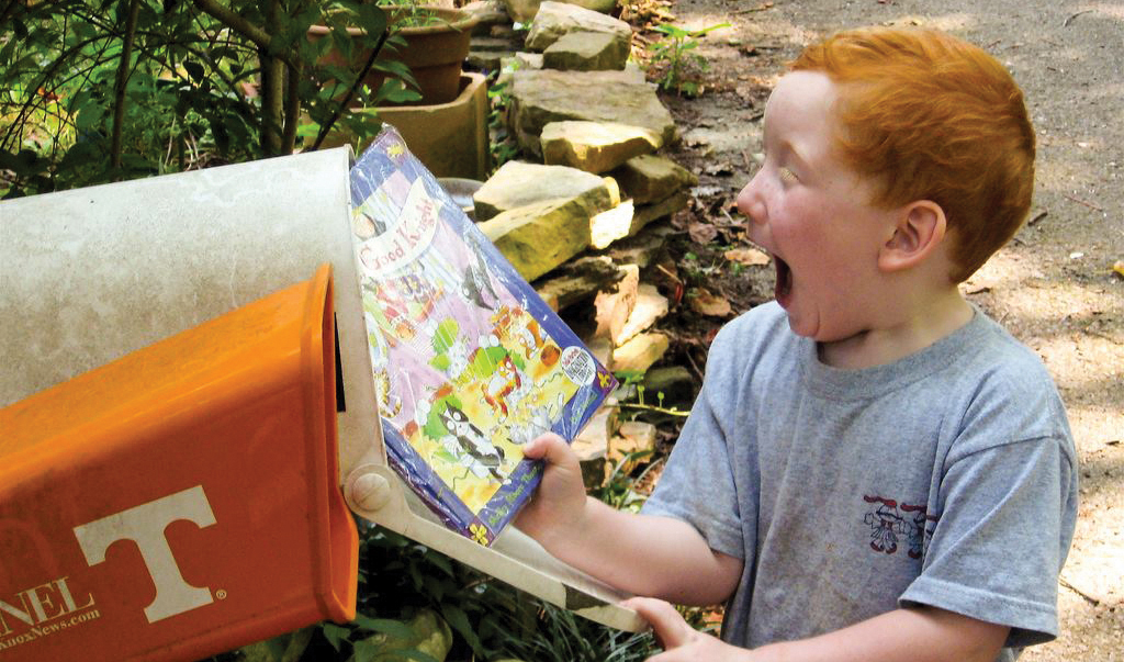 a young boy with a delighted expression on his face, receiving an Imagination Library book from the mailbox